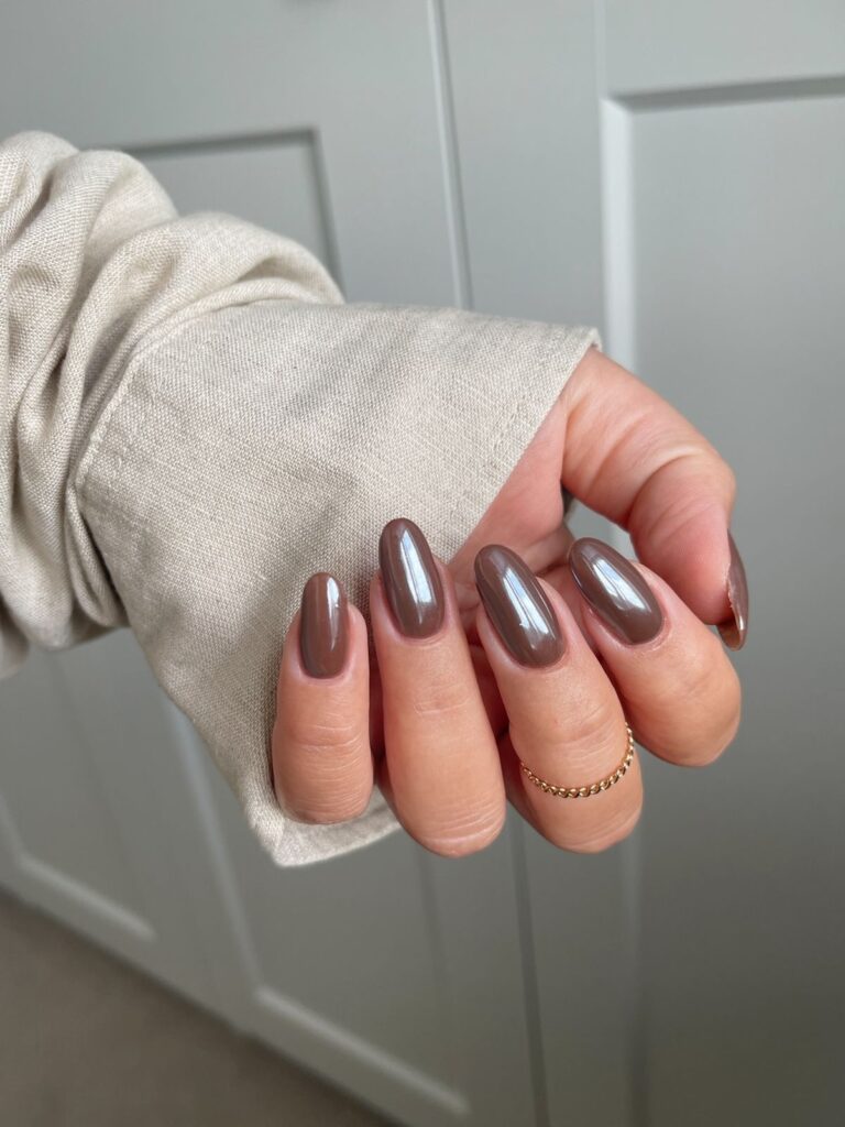 Medium length, almond nails painted with a shimmering espresso brown metallic polish, against a textured neutral background.