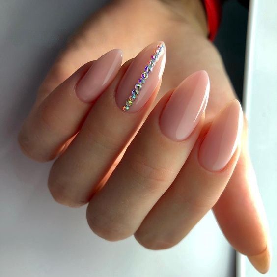 A manicured hand displaying sleek, almond-shaped wedding day nails for bride in a high-gloss, sheer neutral pink, with a single line of tiny, iridescent rhinestones extending down the middle finger.