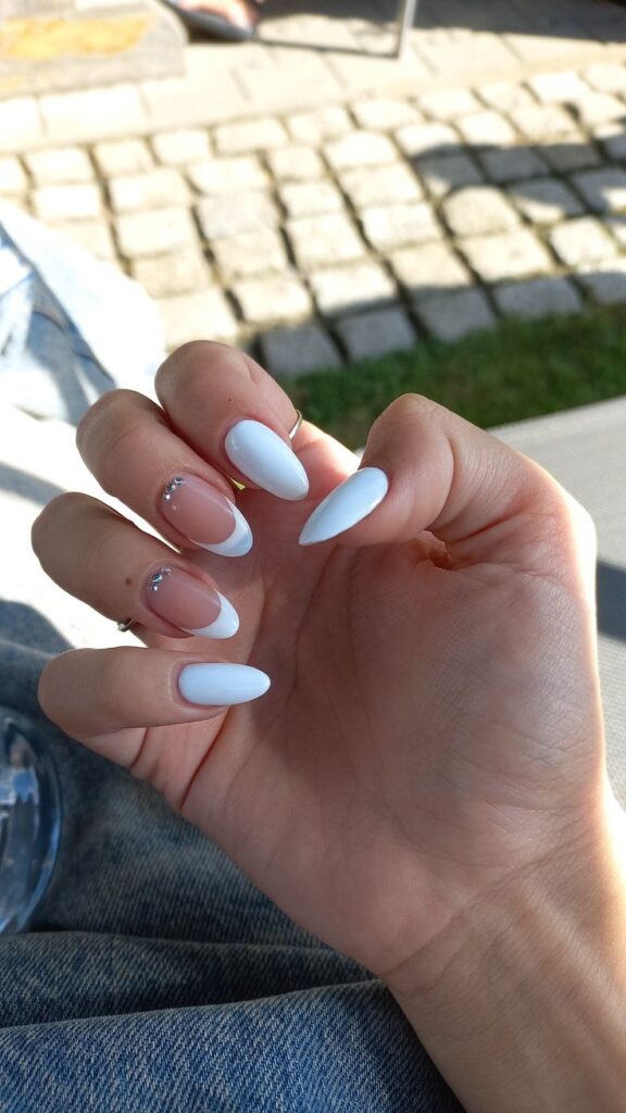 Long, almond-shaped wedding day nails alternating between a solid opaque white polish and a classic French manicure accented with two tiny rhinestones at the cuticle base.