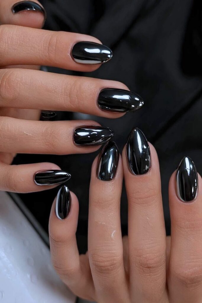 Extremely glossy, almond-shaped black metallic nails against a textured black background.