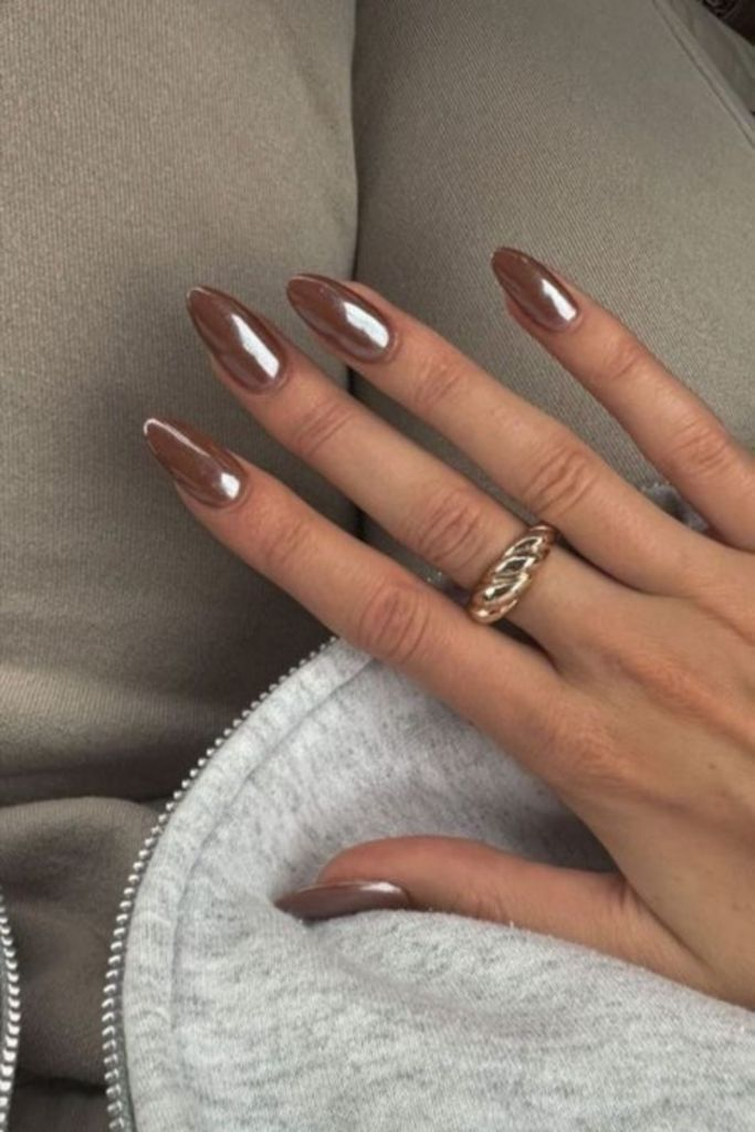Long, almond-shaped nails with a rose-gold or bronze metallic finish, resting on gray fabric.