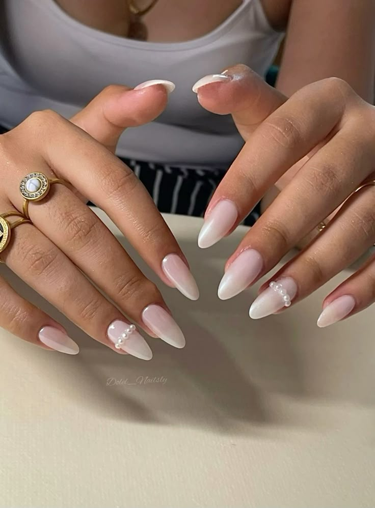 Two hands are held up showcasing long, almond-shaped white ombré wedding day nails, with a neat vertical line of tiny pearls adorning the ring finger.